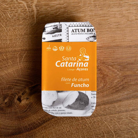 A tin of Santa Catarina tuna in newspaper-style packaging with an orange label against a wood background