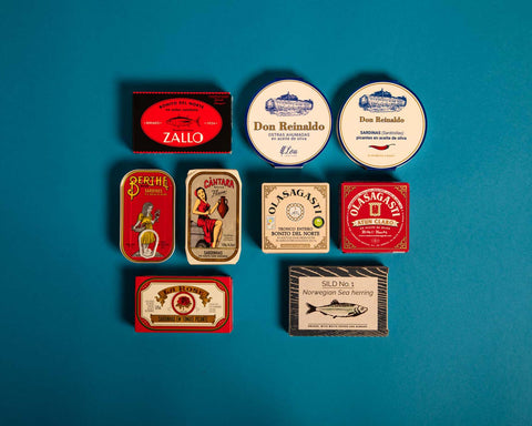 A selection of colourfully-packaged tinned fish against a light blue background.