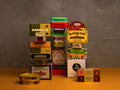 Selection of tins in colourful boxes with different designs and traditional illustrations text on a yellow table against a gray wall
