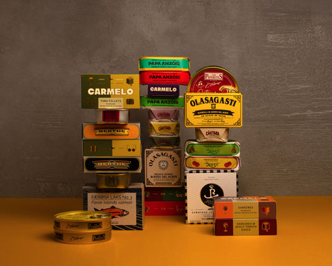 Selection of tins in colourful boxes with different designs and traditional illustrations text on a yellow table against a gray wall