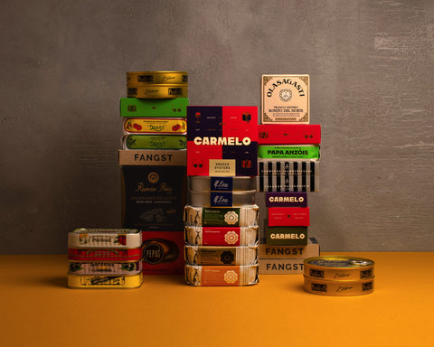 A collection of premium tinned fish products from different brands, presented in boxes and cans, displayed against a yellow background.