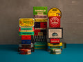 Stack of various tins and boxes with different brand labels on a blue and gray background