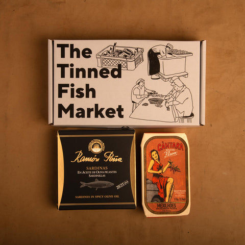 Two tins of fish in striking and colourful packaging beneath an illustrated gift box