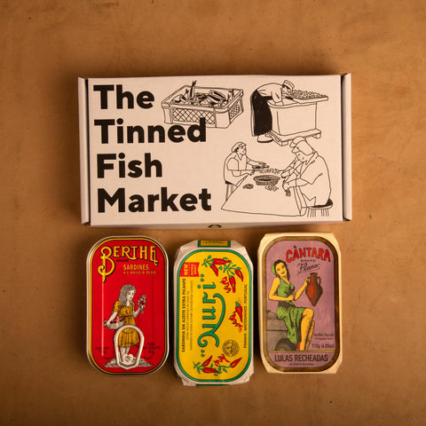 Three colourfully packaged tins of fish next to an illustrated gift box