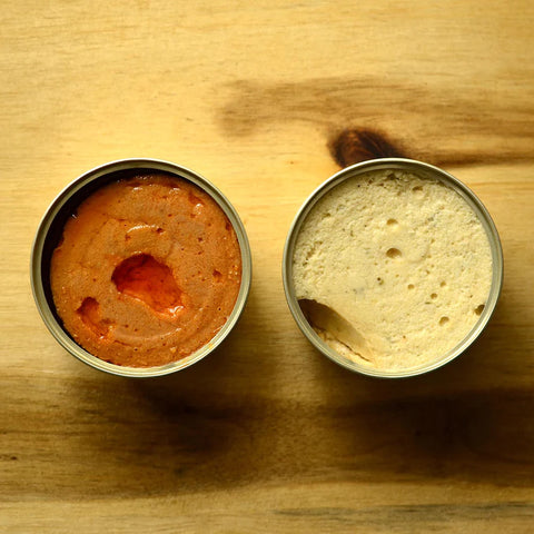 Two open tins of pate - one light orange, one white - against a wooden background.