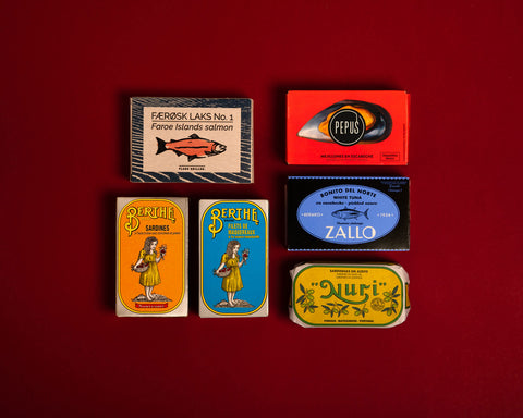 A selection of colourfully-packaged tinned 
sardines, tuna, mackerel, salmon and mussels against a red background.