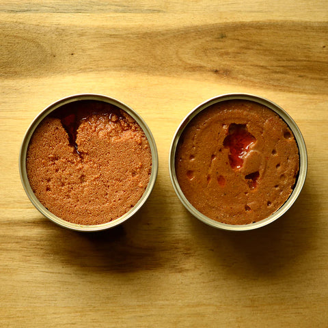 Two open tins of pate, waiting to be savoured on a pinewood table top.