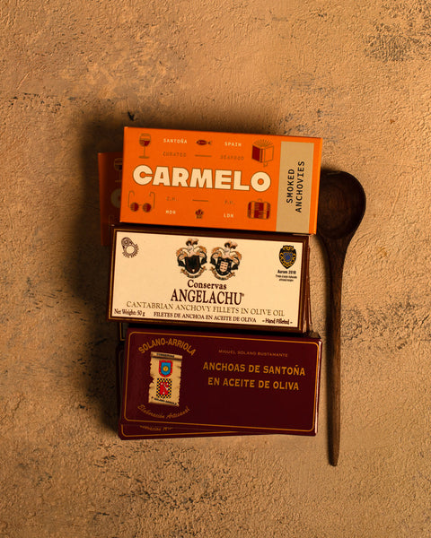 Three tinned fish market anchovy boxes packaging boxes on a textured vintage table with a wooden spoon