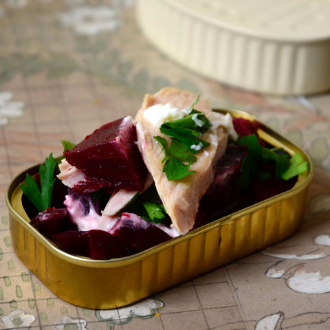 Fillets of tuna placed on top of beetroot and garnished with chopped parsley in a gold trim tin.