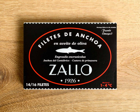 A tin of Cantabrian anchovies in black and red packaging against a light wood background.