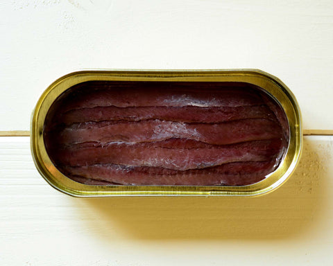 tinned anchovies with gold trimming placed upon a wooden table